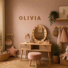 Load image into Gallery viewer, Children's room with wooden vanity, mirror, and decorative items against a pink wall with cork letters spelling Olivia
